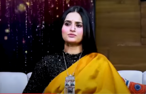 Ukasha Gul Ashraf hosting a TV show, holding a microphone.